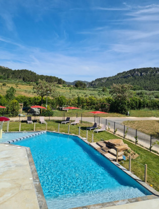 Swimmingpool med liggestole, røde parasoller og udsigt over grønne bakker på Camping De l'Olivigne i Occitanie.