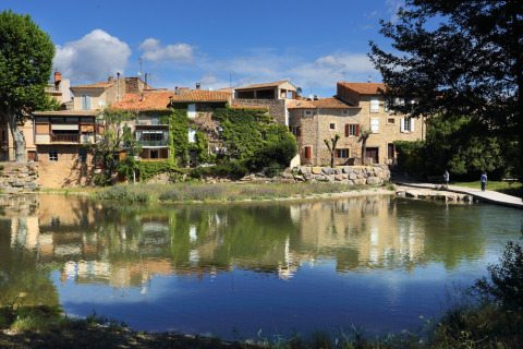 Vista pintoresca de casas junto al río en Camping De l'Olivigne, Occitanie, Francia, con reflejos en el agua.