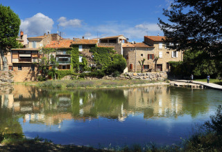 Malermesterudsigt over charmerende rækkehuse langs en flod i Camping De l'Olivigne, Occitanie, Frankrig.