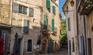 Strada di ciottoli con edifici in pietra e persiane vicino a Bize-Minervois, Occitania, Francia.