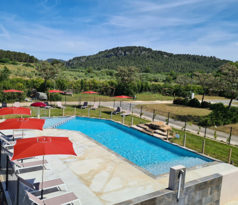Zwembad met rode parasols bij Camping De l'Olivigne in Occitanie, Frankrijk, omringd door groene heuvels.
