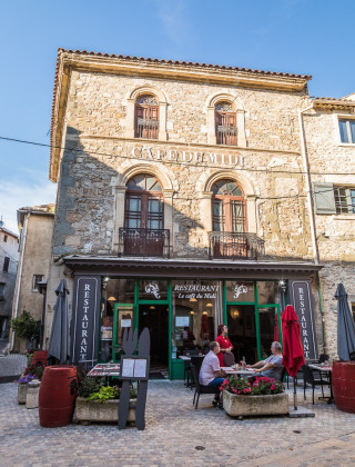 Facciata in pietra del ristorante Le Café du Midi con tavoli all'aperto a Bize-Minervois, Occitanie, Francia.