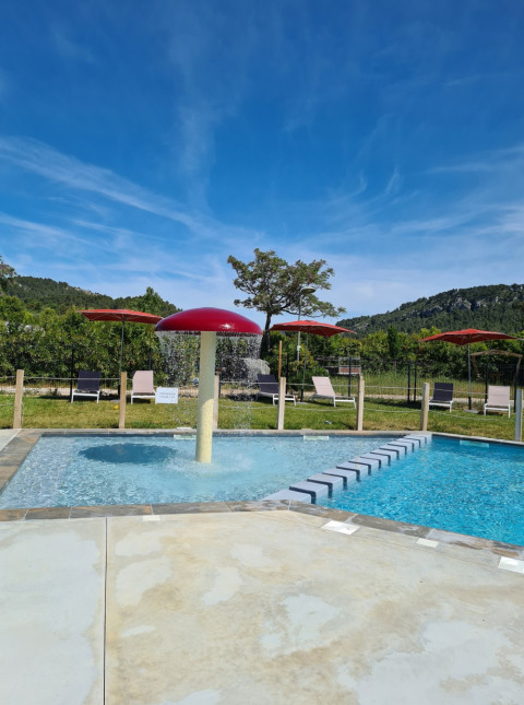 Piscina con seta de agua roja, tumbonas y paisaje natural en Camping De l'Olivigne, Occitania, Francia.