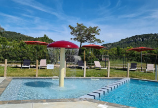 Swimmingpool med rød svampespray, solstole og grønne bakker på Camping De l'Olivigne, Occitanie, Frankrig.
