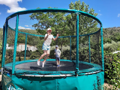 Dos niños saltando en una gran cama elástica con red en Camping De l'Olivigne en Occitania, Francia.