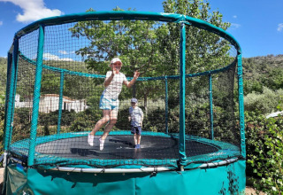 To børn hopper på en stor trampolin med sikkerhedsnet på Camping De l'Olivigne i Occitanie, Frankrig.