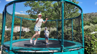 Due bambini saltano su un grande trampolino con rete al Camping De l'Olivigne in Occitania, Francia.