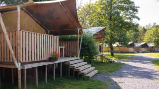 Tienda safari con baño privado en una terraza de madera elevada en un camping rodeado de árboles.