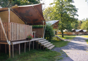 Tenda safari con servizi igienici privati su veranda in legno rialzata in un campeggio immerso nel verde.