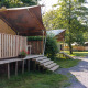 Safari telt med sanitære faciliteter på en hævet træveranda i en grøn campingzone omgivet af træer.