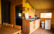 Kitchen area in a safari tent with wooden furniture, gas stove, mini fridge, and outside window.