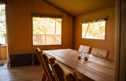 Binnenkant van een safaritent met houten tafel en stoelen op Camping de Chênefleur in België, zonlicht binnen.