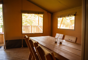 Interior de una tienda safari con mesa y sillas de madera en Camping de Chênefleur, Bélgica, iluminado por el sol.