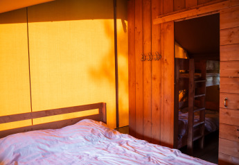 Vista interna di una tenda safari con pareti in legno, letto matrimoniale e letti a castello illuminati.