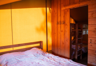 Interior view of a safari tent with wooden walls, a double bed, and bunk beds in warm lighting.