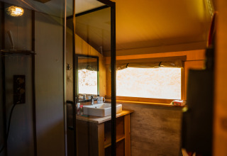 Interiør af Safari-telt med eget badeværelse, håndvask, stort vindue og moderne belysning.
