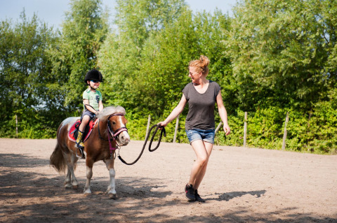Ein Kind reitet auf einem Pony, das von einer Frau geführt wird, bei FarmCamps De Smulhoeve in Nordbrabant.