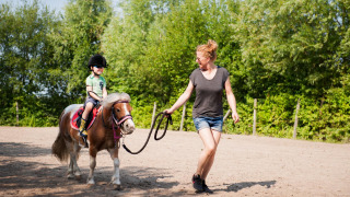 Un niño monta un pony guiado por una mujer en FarmCamps De Smulhoeve, un parque vacacional en Brabante Septentrional.