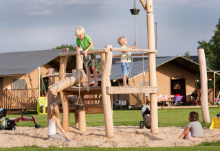 Børn leger på en legeplads med træudstyr på FarmCamps De Smulhoeve feriepark i Nord-Brabant, Holland.