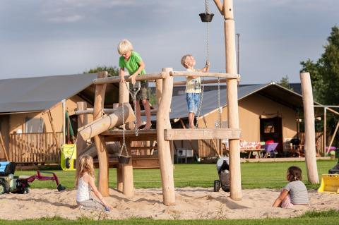Children playing on a wooden playground structure at FarmCamps De Smulhoeve holiday park in North Brabant, Netherlands.