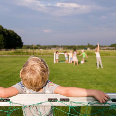 Niño apoyado en una portería mientras otros juegan en el césped en FarmCamps De Smulhoeve, Países Bajos.