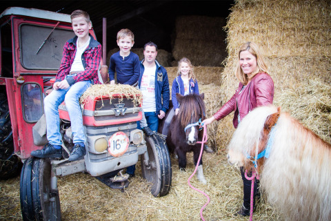 Familie auf einem Bauernhof in Nordbrabant mit Kindern auf dem Traktor und Ponys neben Heuballen.