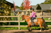Kind reitet Pony mit Reithelm auf umzäuntem Gelände bei FarmCamps De Smulhoeve, Ferienpark in Nordbrabant, Niederlande.