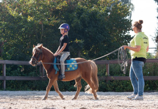 Een kind rijdt op een pony onder toezicht van een instructrice bij FarmCamps Breehees in Noord-Brabant.