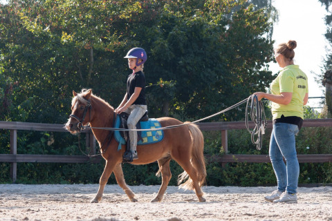 Ein Kind reitet auf einem Pony unter Anleitung eines Betreuers im FarmCamps Breehees in Nordbrabant, Niederlande.