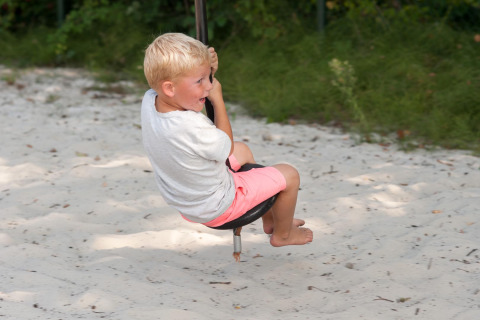 Niño jugando descalzo en un columpio sobre arena en FarmCamps Breehees, parque vacacional de North-Brabant, Países Bajos.