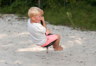 Boy playing barefoot on a swing over sand at FarmCamps Breehees holiday park in North-Brabant, Netherlands.