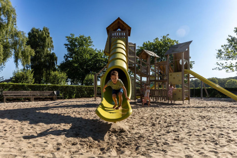 Kinderen spelen op een speeltuin met gele glijbaan in FarmCamps Breehees in Noord-Brabant, Nederland, vakantiepark.