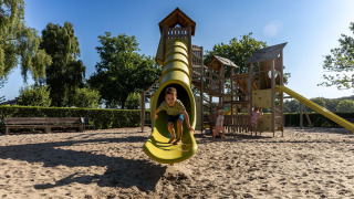 Niños juegan en un parque infantil con tobogán amarillo en FarmCamps Breehees, parque vacacional en Brabante Septentrional.