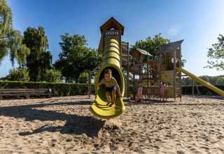 Børn leger på en legeplads med rutsjebane i sand, FarmCamps Breehees, en feriepark i Nord-Brabant, Holland.