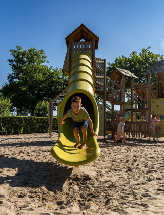 Niños juegan en un parque infantil con tobogán amarillo en FarmCamps Breehees, parque vacacional en Brabante Septentrional.