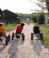 Niños montan en karts por un sendero de tierra en FarmCamps Breehees, parque vacacional en Brabante Septentrional.