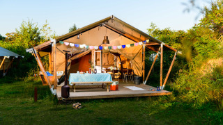 Safari tent with wooden deck, colorful bunting, and outdoor dining table set in lush green nature.
