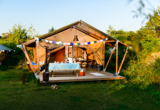 Tienda de safari con terraza de madera, guirnaldas coloridas y mesa de comedor en plena naturaleza.
