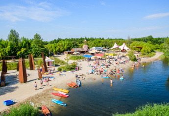 Glampingverblijf met zandstrand, kajaks, zwemmers en tenten aan een meer, omgeven door groene bomen.