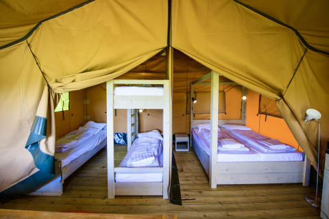 Innenansicht eines Safarizelts mit Holzboden, Doppelbett, Etagenbett und Einzelbetten für Gäste.