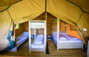 Interior de una tienda safari con suelo de madera, cama doble, litera y camas individuales listas para huéspedes.