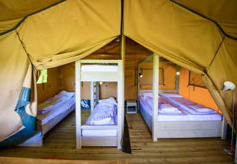 Interior de una tienda safari con suelo de madera, cama doble, litera y camas individuales listas para huéspedes.
