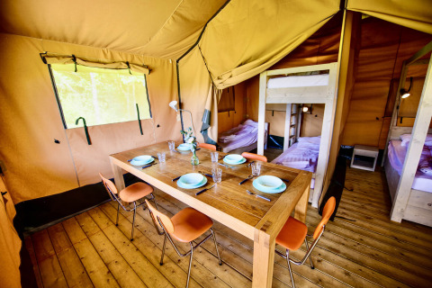 Interior de tienda safari con mesa de comedor de madera, sillas y áreas de descanso con camas.