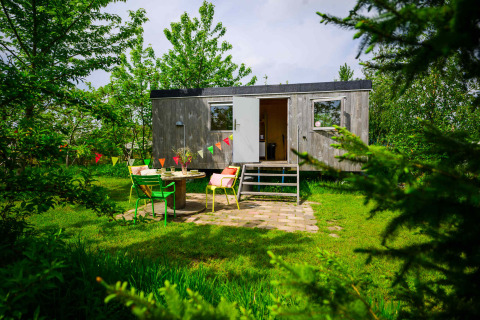 Pequeña casa Pipowagen en Netl Camping Kallumaan, Países Bajos, con jardín y coloridas sillas afuera.