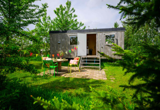 Pequeña casa Pipowagen en Netl Camping Kallumaan, Países Bajos, con jardín y coloridas sillas afuera.