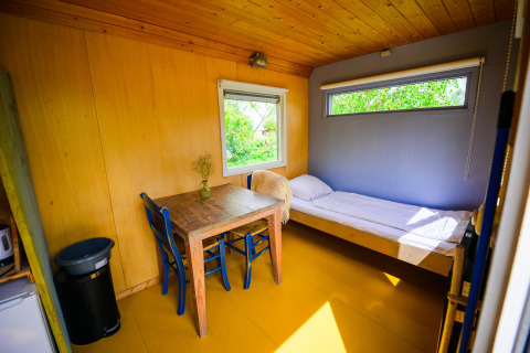 Intérieur de la tiny house Pipowagen au Netl Camping Kallumaan, Pays-Bas, avec lit et table.