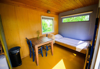Interior de la tiny house Pipowagen en Netl Camping Kallumaan, Países Bajos, con cama y mesa.