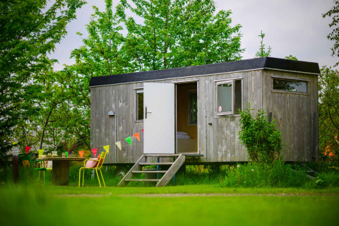 Charming Pipowagen tiny house at Netl Camping Kallumaan in the Netherlands, set among lush green trees.
