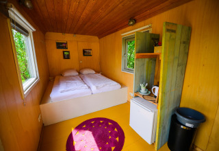 Acogedor interior de Pipowagen tiny house con dos camas, zona de cocina y ventanas luminosas.