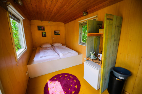 Intérieur chaleureux de la tiny house Pipowagen avec deux lits, kitchenette et fenêtres donnant sur la nature.